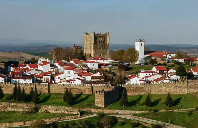 Imagem aréa da paisagem de Bragança, onde se vê o castelo, a moralha e vários edifícios, num dia com algumas núvens.
