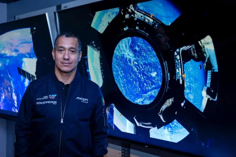 Fotografia de Emiliano Ventura à frente de dois ecrãs onde estão imagens espaciais