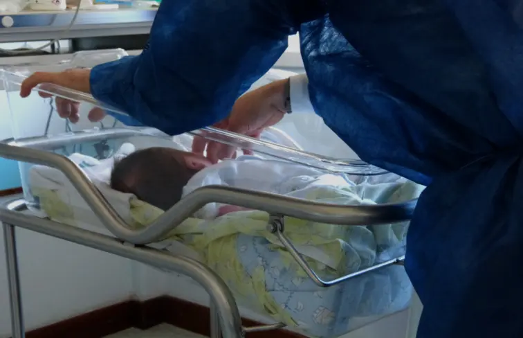 Bebé está deitado no berço do hospital enquanto um adulto o acaricia